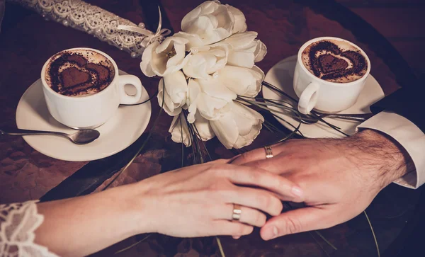 Zwei Tassen Kaffee und die Hand von Braut und Bräutigam mit Trauringen Stockbild