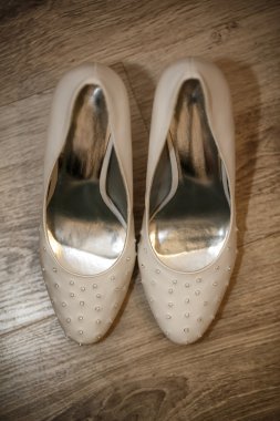 Close up of white elegant and stylish bridal shoes on the wooden floor