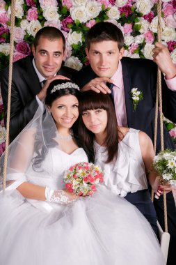 Happy bride and groom  with bridesmaids and groomsmen in studio background from flowers