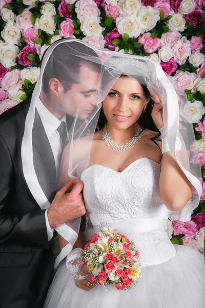Счастливая невеста и жених в студии фон из цветов — стоковое фото
