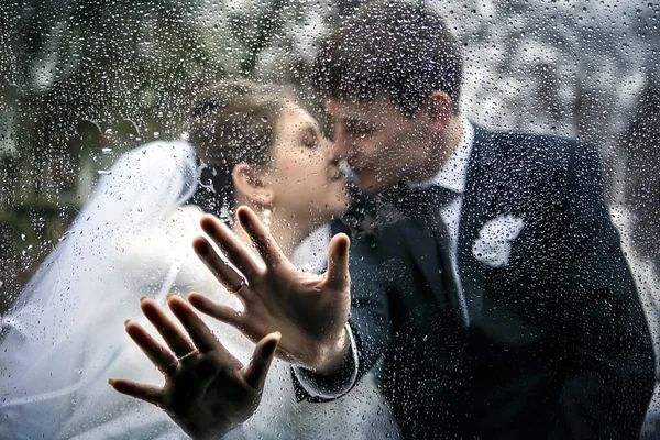 the hands of a bride and a groom on the car window with drops from a rain on the background a kiss of the groom and the bride