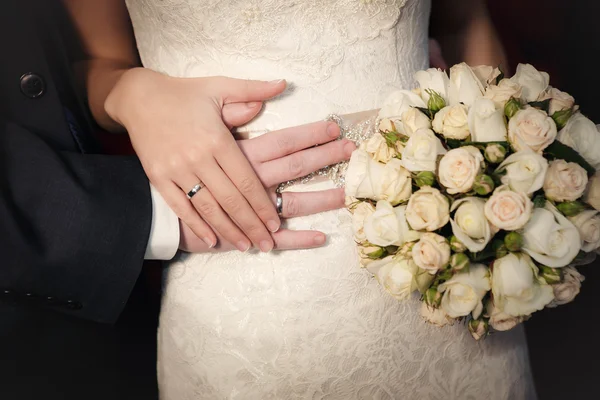 Las manos del novio y la novia con anillos de boda y un ramo de boda de rosas —  Fotos de Stock