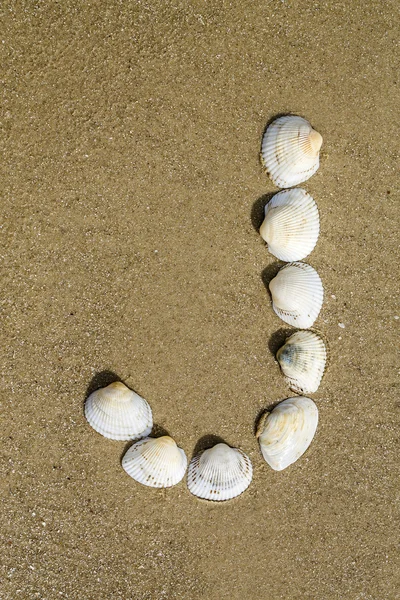 Sorunsuz kum zemin üzerine deniz kabukları kullanılarak yapılan alfabesi — Stok fotoğraf