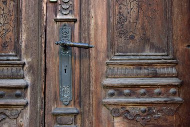 Old brown wooden door of an old house with ornate carvings and ornaments and doorknobs made of metal - antique and antiquity