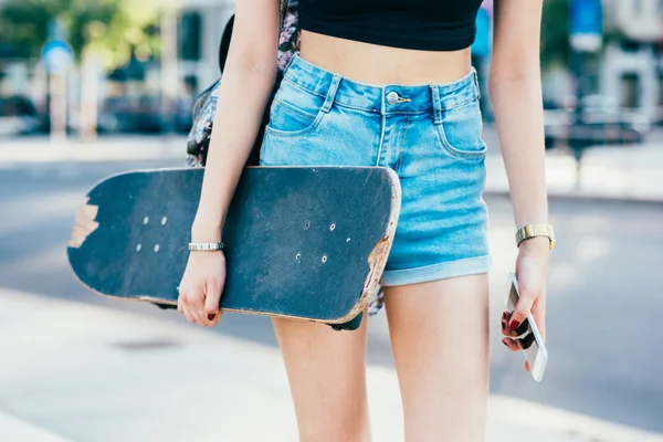 Žena držící skateboardu a chytrý telefon — Stock fotografie