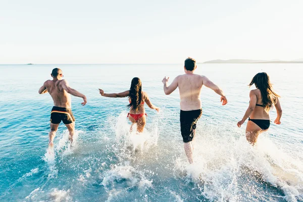 Amigos multiétnicos corriendo en la playa hacia el mar — Foto de Stock