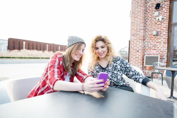 Women sitting on a bar, using smartphone — Stock Photo, Image