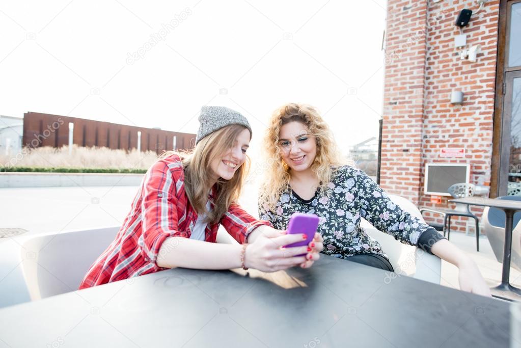 women sitting on a bar, using smartphone