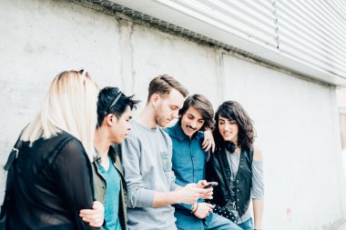 çok ırklı arkadaşlar Smartphone kullanarak duvara yaslanmış