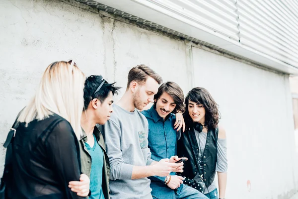 Amigos multiétnicos apoyados en la pared usando un teléfono inteligente — Foto de Stock