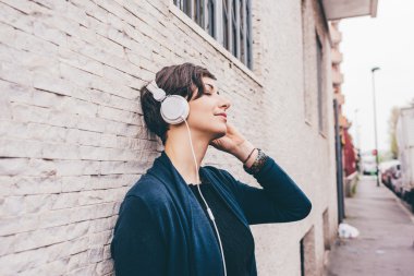 woman leaning against a wall, listening music