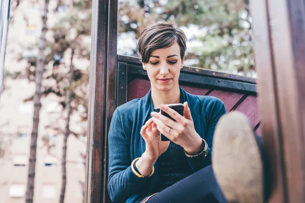 Femme assise dans un playgragara tenant un téléphone intelligent — Photo
