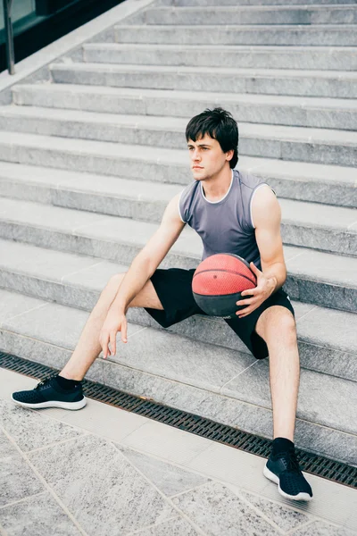 man sitting on a staircase holding a basket ball