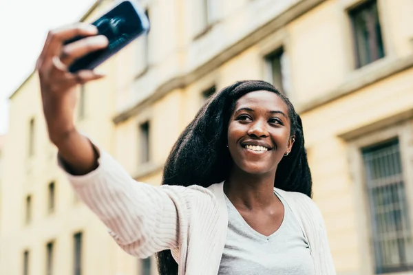 Mujer sosteniendo teléfono inteligente tomando selfie — Foto de Stock