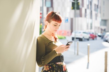 woman leaning against wall holding smartphone