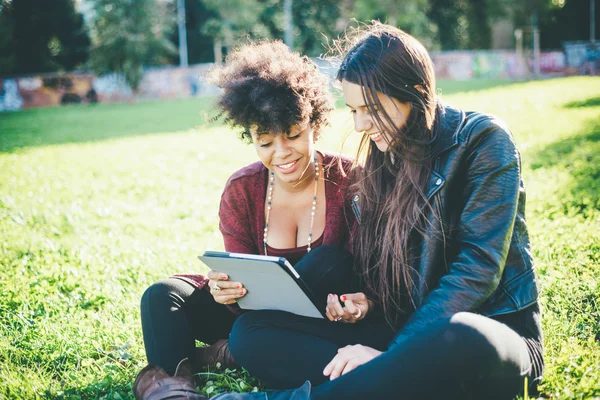 Women using tablet sitting in park — Stock Photo, Image