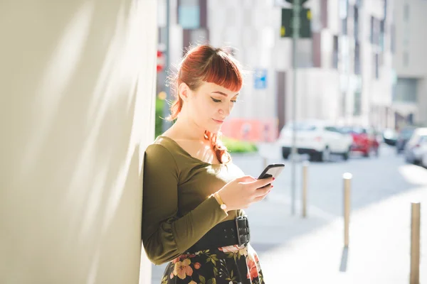 Woman leaning against wall holding smartphone — Stockfoto