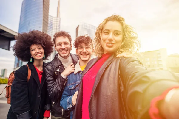 Group of multiethnic friends outdoor having fun and taking selfie using smartphone outdoor in the cty with skyscrapers