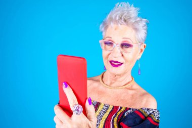 Olgun Kafkasyalı büyükanne kadın akıllı telefon kullanarak izole edildi. Video veya video izleyerek aile dostlarını mavi arka planda aramak - internet, eğlence, teknoloji kavramı