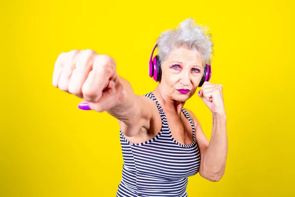 Elderly determinated woman practicing boxing on yellow background learning how to defend herself - sport, protection, security concept