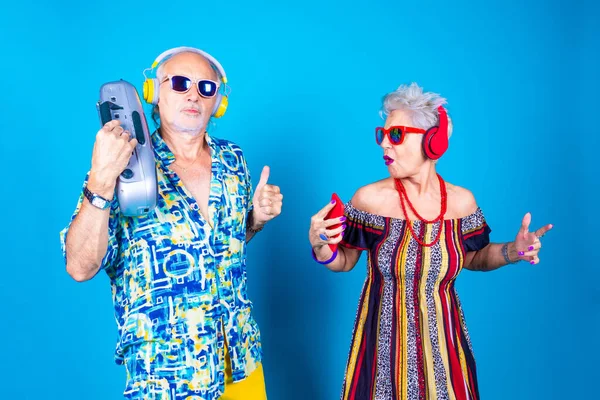 Couple of senior grandpa and grandma man and woman on blue background clubbing isolated with stereo and smartphone - technology, clubbing, having fun concept