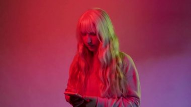 Stüdyoda, kırmızı arka planda yaşayan beyaz bir kadının, izole edilmiş akıllı telefon kullanarak sosyal medyaya bağımlı olma eğilimlerinin keyfini çıkarırken çekilmiş bir fotoğrafı.