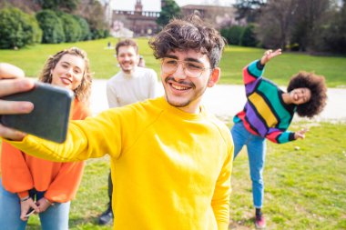 Farklı etnik gruplardan dört kişi, dışarıda akıllı telefon kullanarak eğleniyor. Selfie çekerken, sosyal mesafeye 2 metre mesafede. 