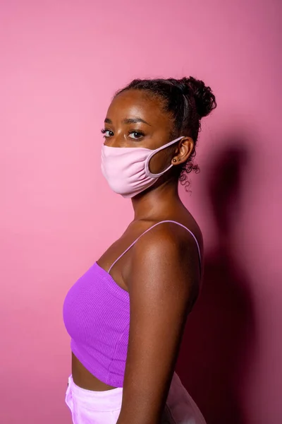 肖像外科的マスクを身に着けている若い黒人女性は ピンクの背景に隔離されたコロナウイルスの拡散から医療を保護します — ストック写真