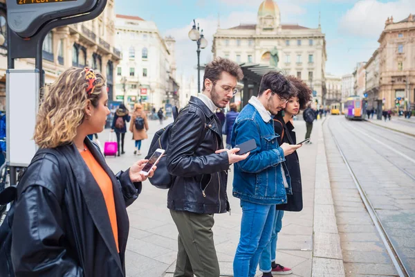4人の友人のグループ多民族の男性と女性は スマートフォンの携帯電話を使用して通勤を停止し お互いに社会的傾向に中毒を無視笑顔待っている — ストック写真