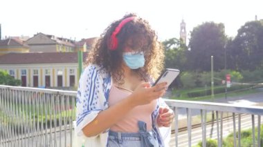 Ağır çekimde, çeşitli etnik çeşitlilikte genç bir kadın elinde bluetooth kablosuz kulaklık ile internet üzerinden müzik dinliyor.