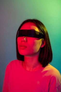 Genç Asyalı kadın renkli arka planda akıllı gözlük takıyor artırılmış gerçekliğin tadını çıkarıyor.