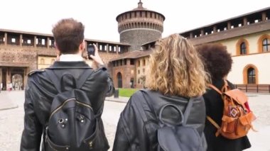 Bir grup turist, Sforzesco Kalesi 'nin önünde Milano' da akıllı telefon kullanarak fotoğraf ya da selfie çekiyor. Tatilde gezintilerin keyfini çıkarıyorlar.