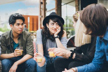 Dört etnik gruptan oluşan bir grup açık hava kulübünde oturup sohbet ediyor ve birlikte iyi vakit geçiriyorlar.