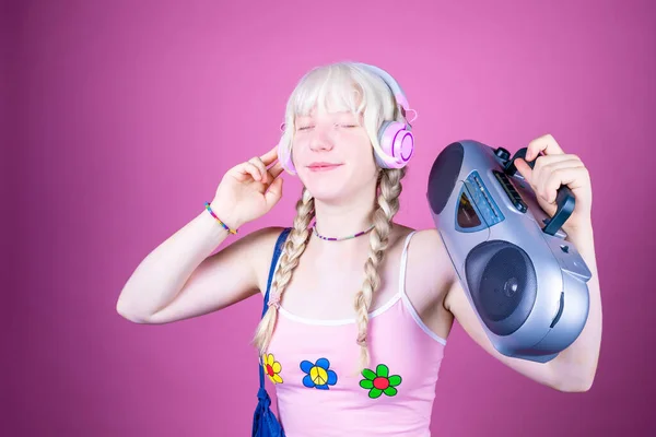 Young beautiful caucasian woman dancing indoor on pink background holding vintage stereo holding vintage radio