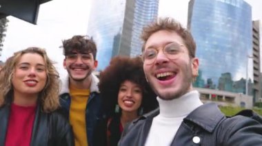 Bir grup çok ırklı arkadaş dışarıda eğleniyor ve şehirde akıllı telefon kullanarak selfie çekiyorlar.
