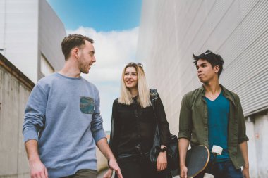 Üç çok ırklı arkadaş, erkek ve kadın birlikte yürüyorlar, sohbet ediyorlar ve birlikte eğleniyorlar.