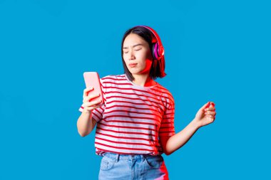 Genç, güzel Asyalı bir kadın, mavi bagette coşkulu bir şekilde dans ediyor. Akıllı telefonu tutuyor, kulüplere gidiyor, müzik dinliyor.