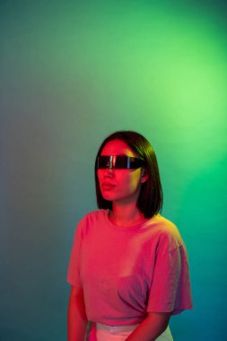 Genç Asyalı kadın renkli arka plan video oyunlarında akıllı gözlük takıyor ya da artırılmış gerçekliğin tadını çıkarıyor.