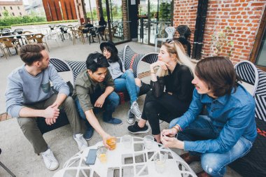 Dört etnik gruptan oluşan bir grup açık hava kulübünde oturup sohbet ediyor ve birlikte iyi vakit geçiriyorlar.