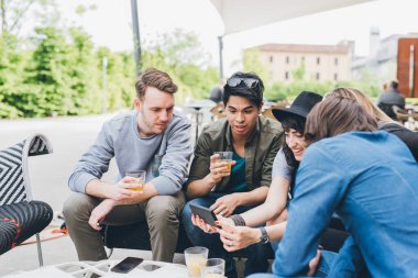 Çok ırklı bir grup arkadaş barda oturup akıllı telefon kullanarak sosyal medyada birlikte eğleniyorlar.