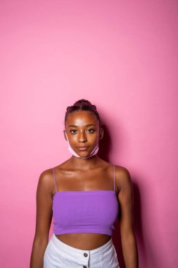 Maske takan genç bir kadın yanlış bir şekilde pembe arka planda izole edilmiş boynunun altında hijyenik olmayan bir şekilde.