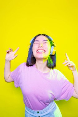 Sarı arka planda izole edilmiş gülümseyen genç bir kadın müzik dinliyor. Heyecanlı ve kablosuz kulaklık takıyor.