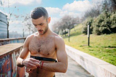Genç sportif beyaz adam kalp atışlarını kontrol ediyor. Akıllı takip cihazıyla.