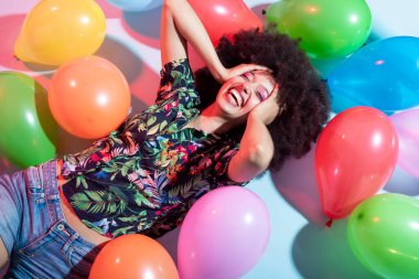 Genç, çok ırklı bir kadın stüdyosu balonla poz verip eğleniyor, gamsız ve pozitif gülüyor.