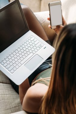 Close up back view young beautifiul asiatic woman indoors using computer and smartphone sitting armchair 