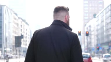 Back view young caucasian businesslike man walking looking around outdoor in the city