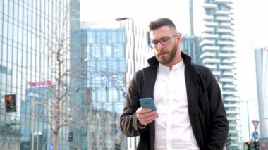 Slow motion young caucasian bearded business man outdoor using smartphone handhold stopping and staring at the camera