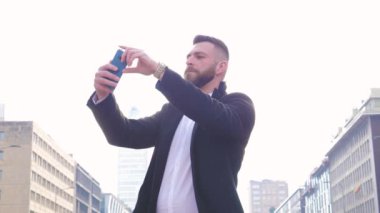 Slow motion young bearded caucasian businesslike man outdoor using smartphone taking selfie or taking pictures making memories as a traveller