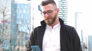 Slow motion young caucasian bearded business man outdoor using smartphone handhold stopping and staring at the camera