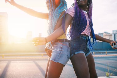İki genç siyah kız kardeş dışarıda müzik dinliyorlar. Kablosuz kulaklıklarla arka planda coşkuyla dans ediyorlar. 